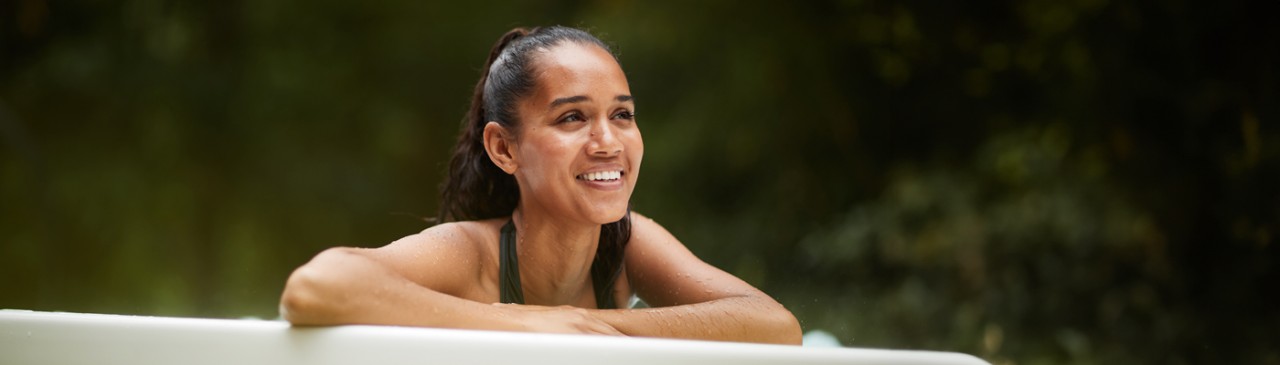 Woman leaning on the edge of a hot tub looking out to the forest.