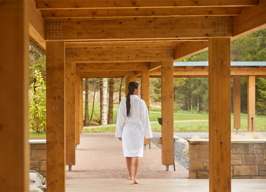Woman walking in a spa robe under a pergola.
