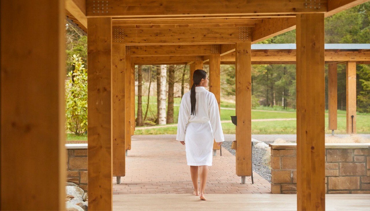 Woman walking in a spa robe under a pergola.