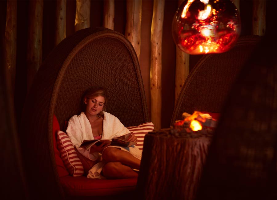 woman reading magazine on comfy seat in front of fire 