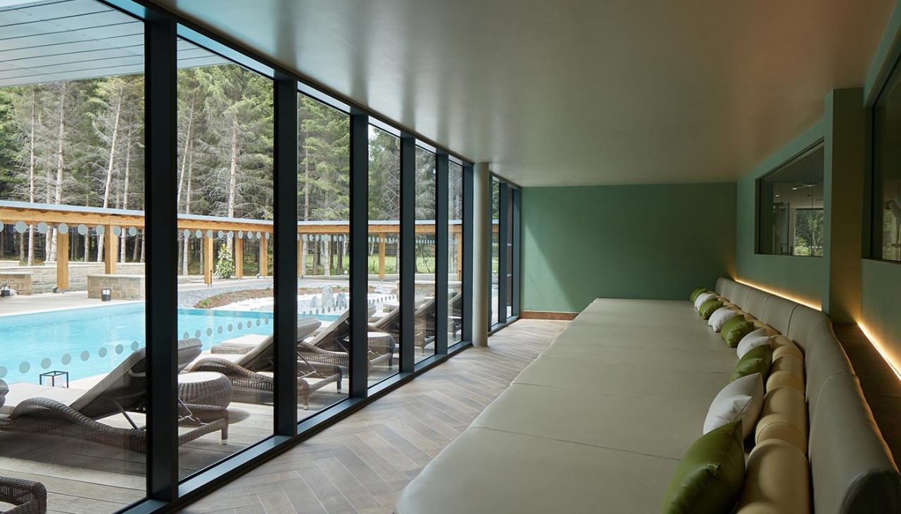 Curved lounging beds with a view of an outdoor pool and the surrounding forest.