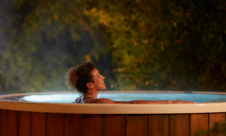 Woman soaking in an outdoor hot tub surrounded by the forest.
