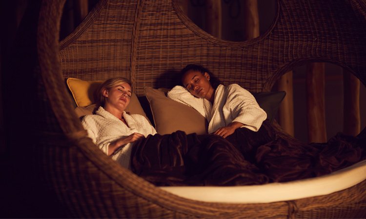Two women snuggled under a blanket in a relax area.