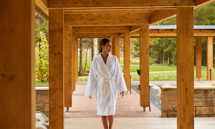 Woman dressed in a spa robe walking under pergola.