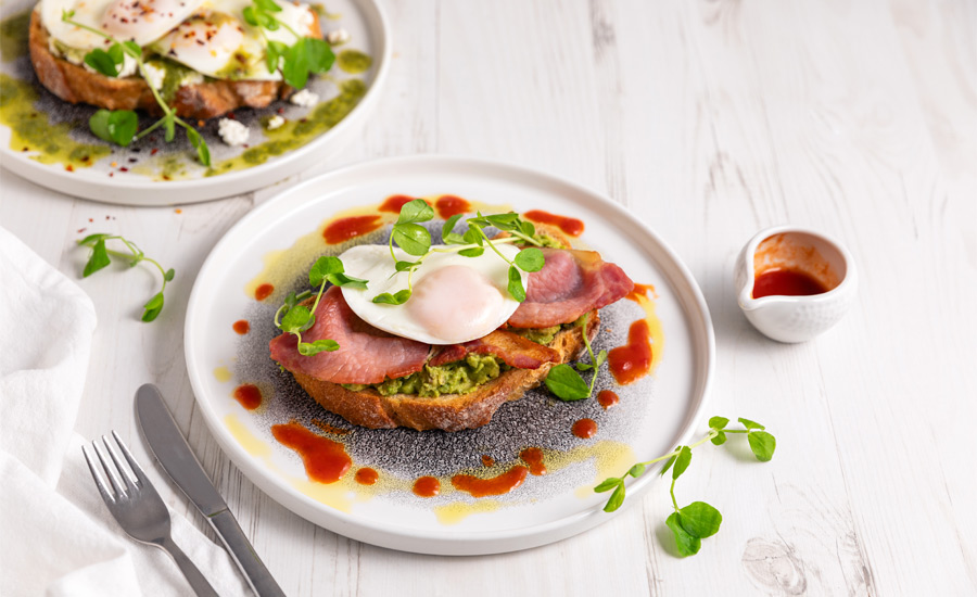 Smashed avocado on sourdough toast, topped with a fried egg and crispy bacon.