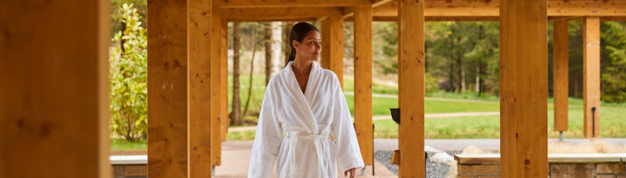 Woman walking dressed in a spa robe under a pergola.