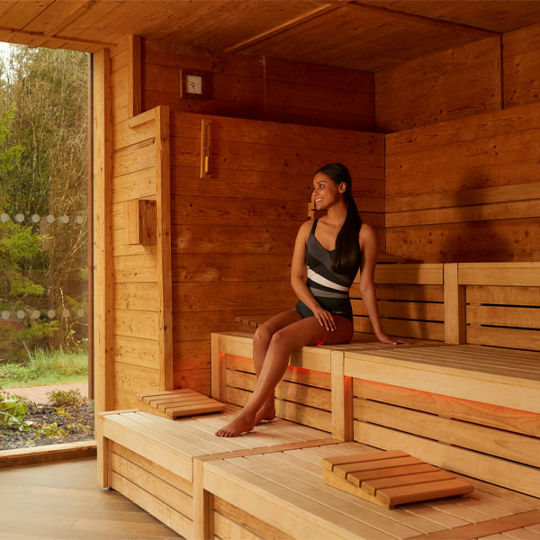 Woman sitting in a Nordic Sauna looking out to the forest.