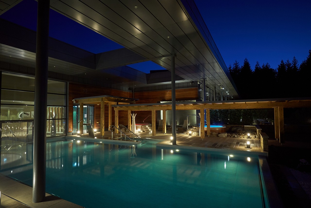 Outdoor Pool in the evening with a pergola lit by outdoor lighting.