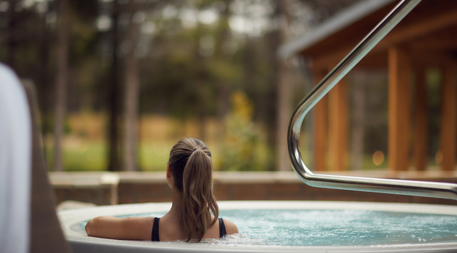 Woman soaking in an outdoor hot tub looking out to the surrounding forest.