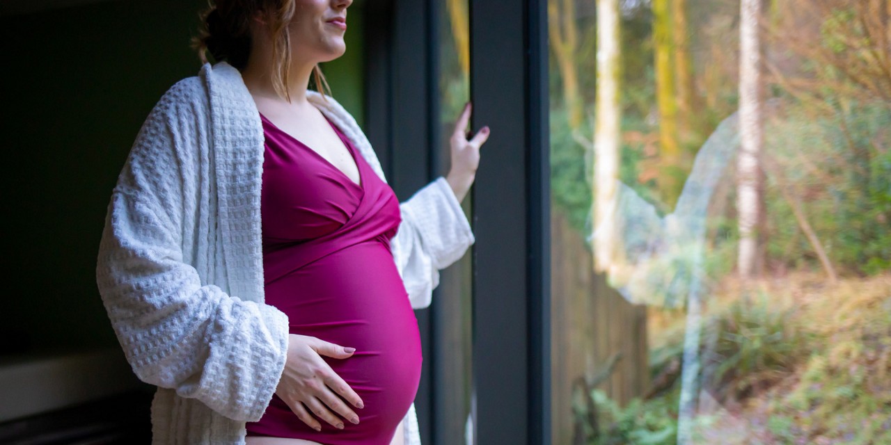 Woman touching her bump as she looks out at the forest.