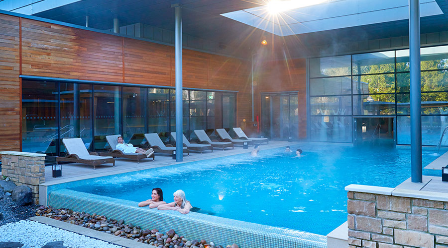 People swimming in an outdoor pool surrounded by loungers. 