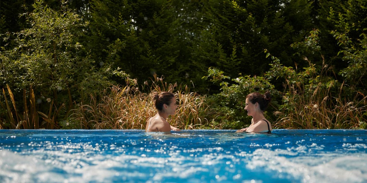 two women in outdoor pool in front of forest