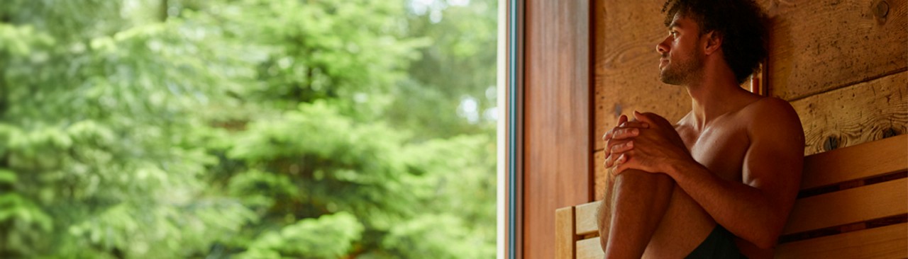 Man sitting in the Nordic Sauna enjoying the forest views.