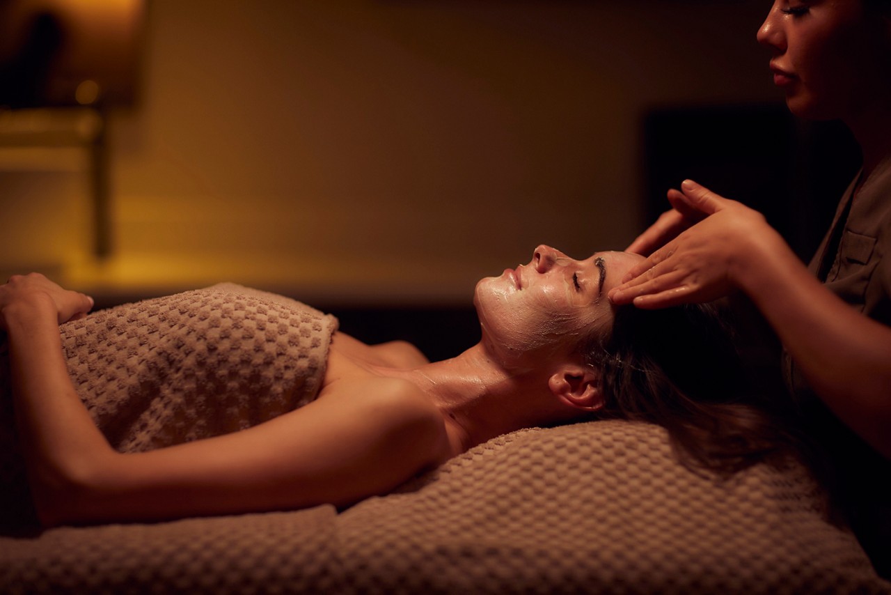 A spa therapist giving a facial treatment to client lying on a spa bed