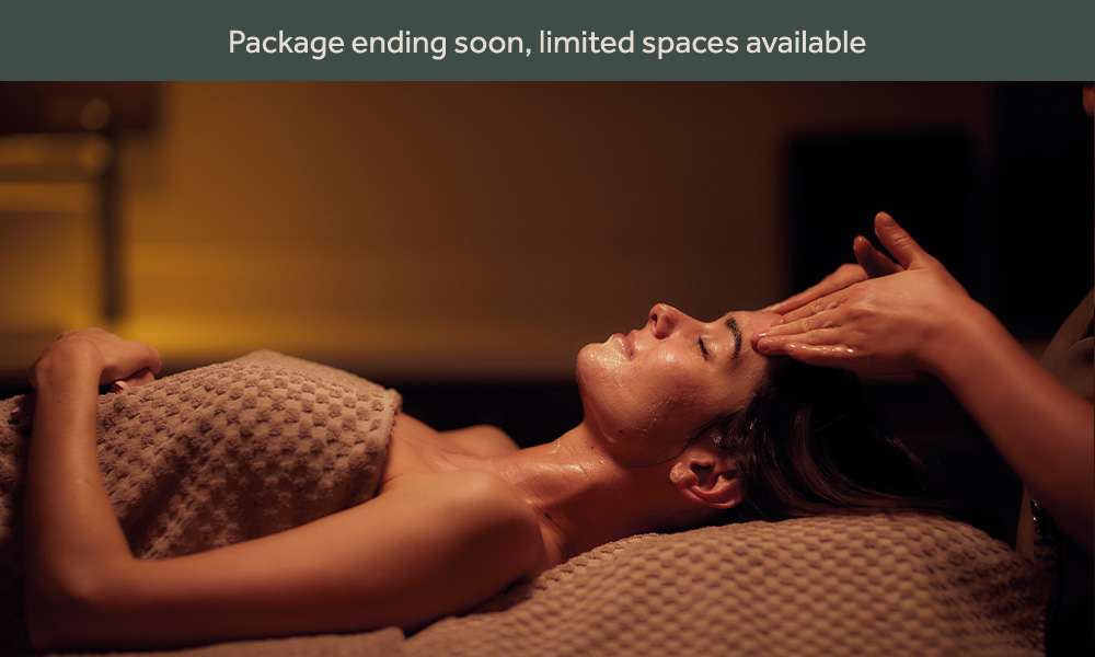 a women lying on a spa be with a towel over her having a facial in a dimly lit room