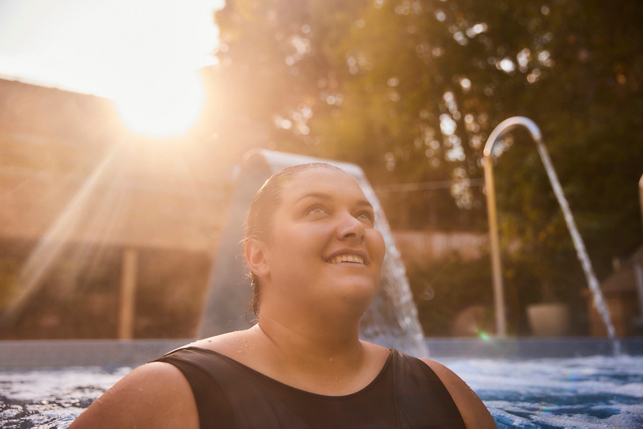 Women un a black swimsuit in a an outdoor pool surrounded by forest
