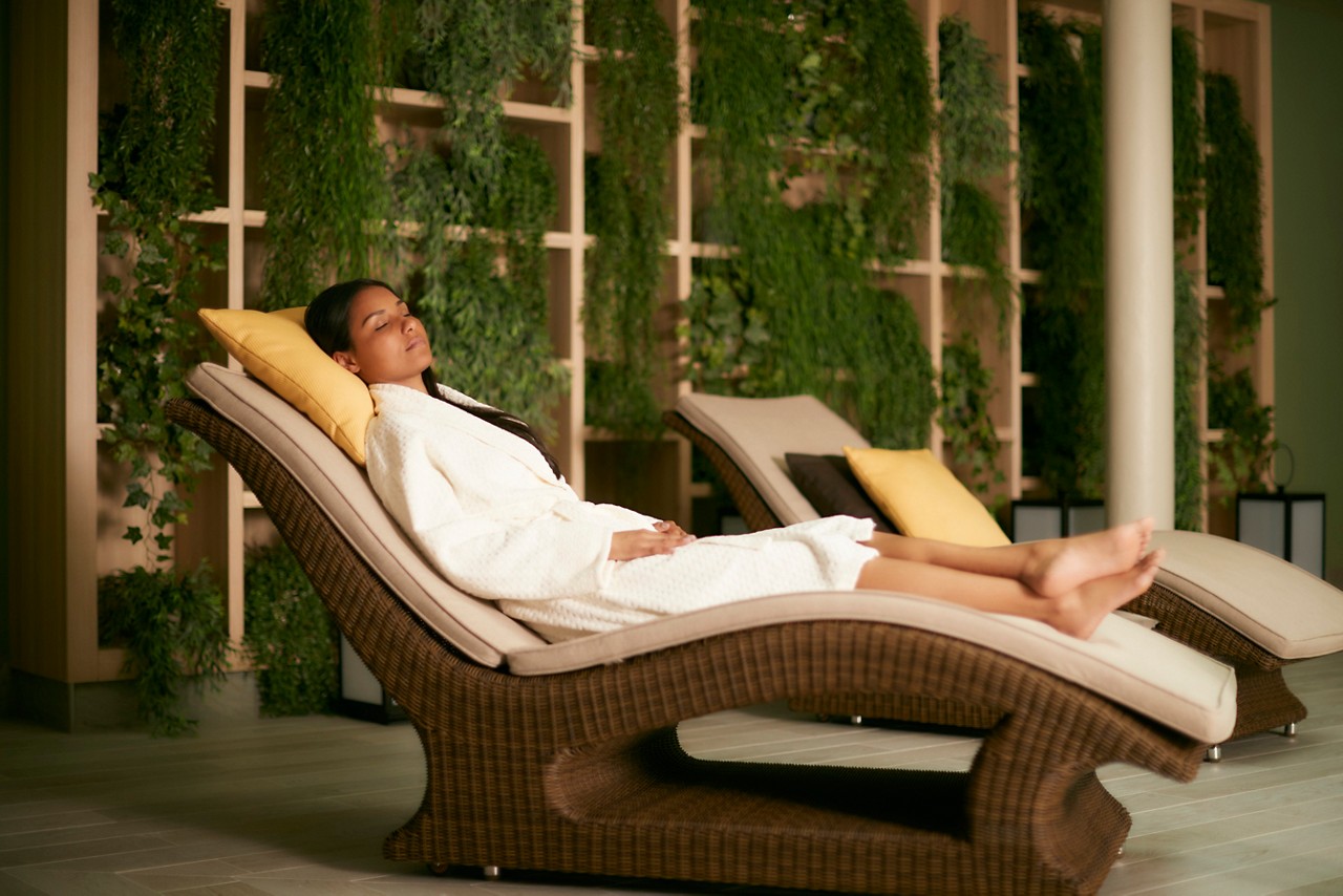 Woman wearing a soft spa robe relaxing on a cushioned lounging bed in the Forest Garden.