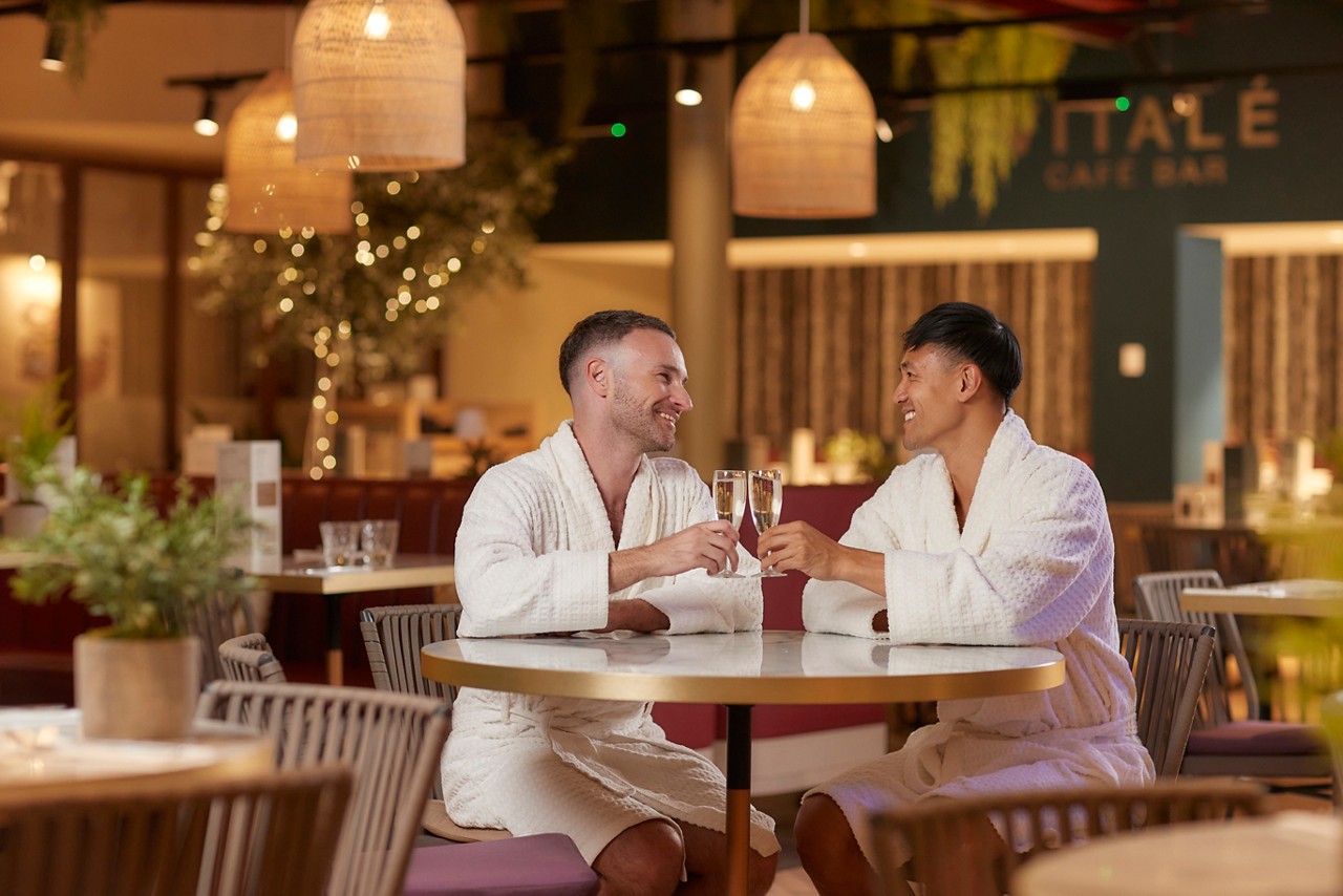 Two people sat at a table in spa robes with prosecco