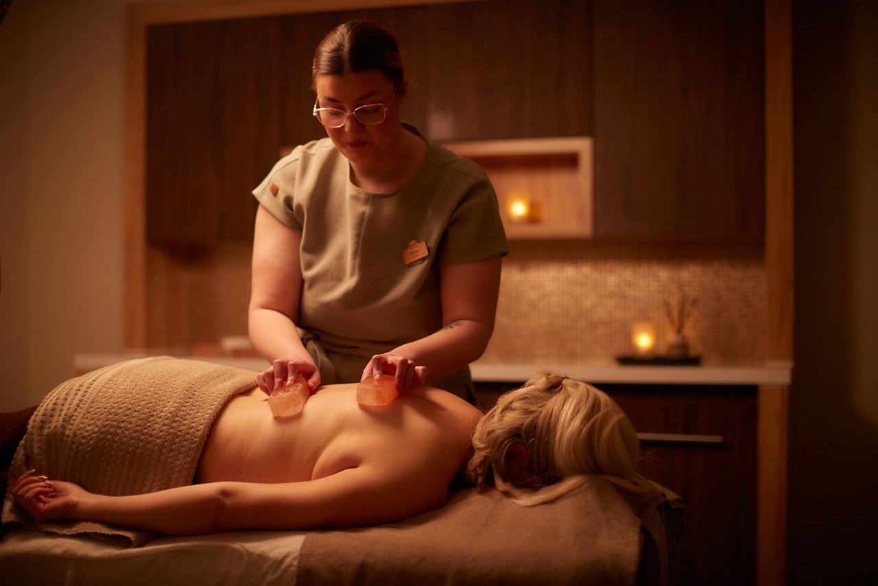 A massage therapist performing a comfort zone Himalayan salt ritual on a clients back