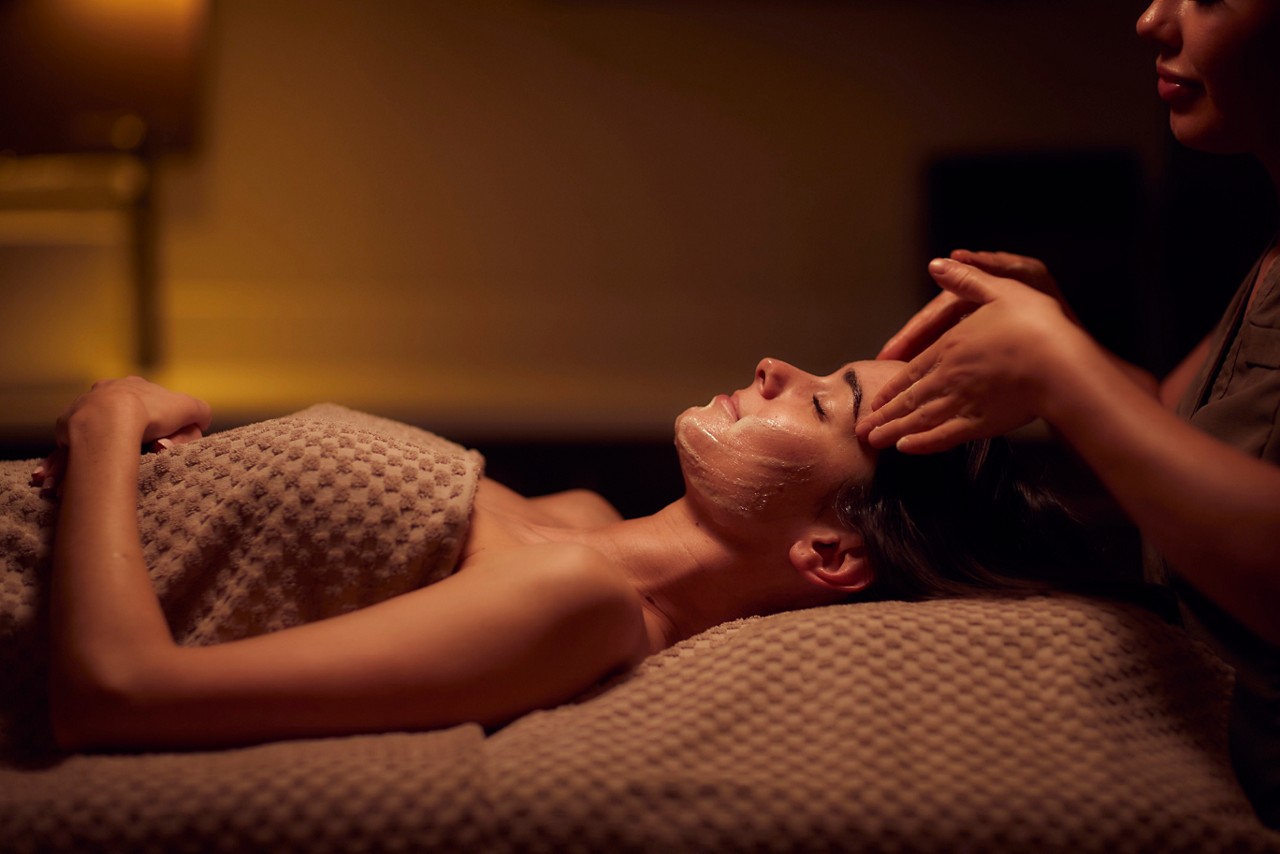 A spa therapist giving a facial treatment to client lying on a spa bed