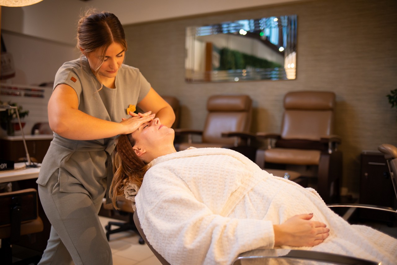 A therapist giving a facial treatment to a client in a spa robe reclining in a spa chair