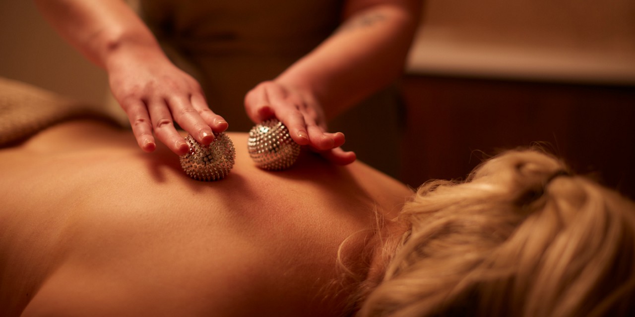 Metal balls being rolled across a woman's back.