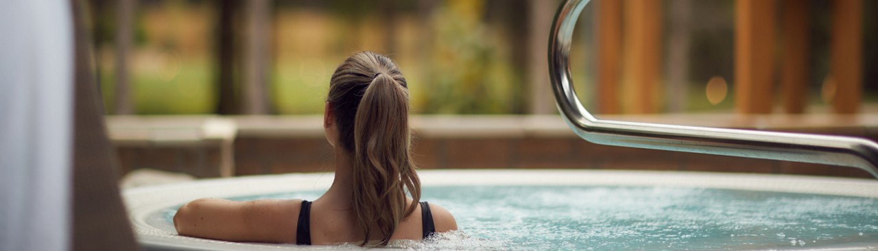 Woman looking out to the forest sitting in a bubbling hot tub.