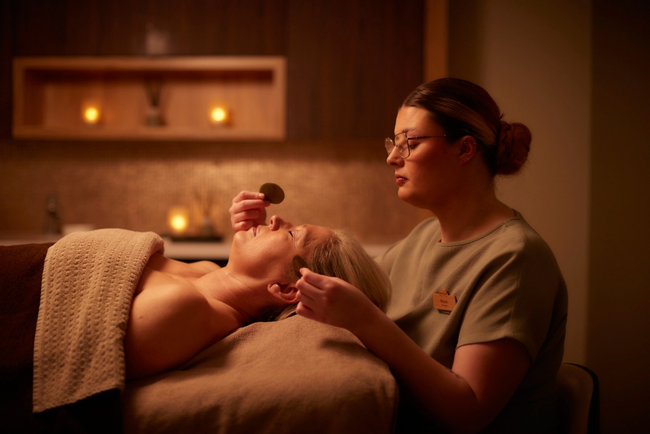 A massage therapist performing a VOYA stress recovery facial treatment on a client lying down