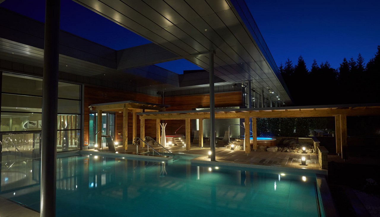 Outdoor pool in the evening with a pergola lit by outdoor lighting.