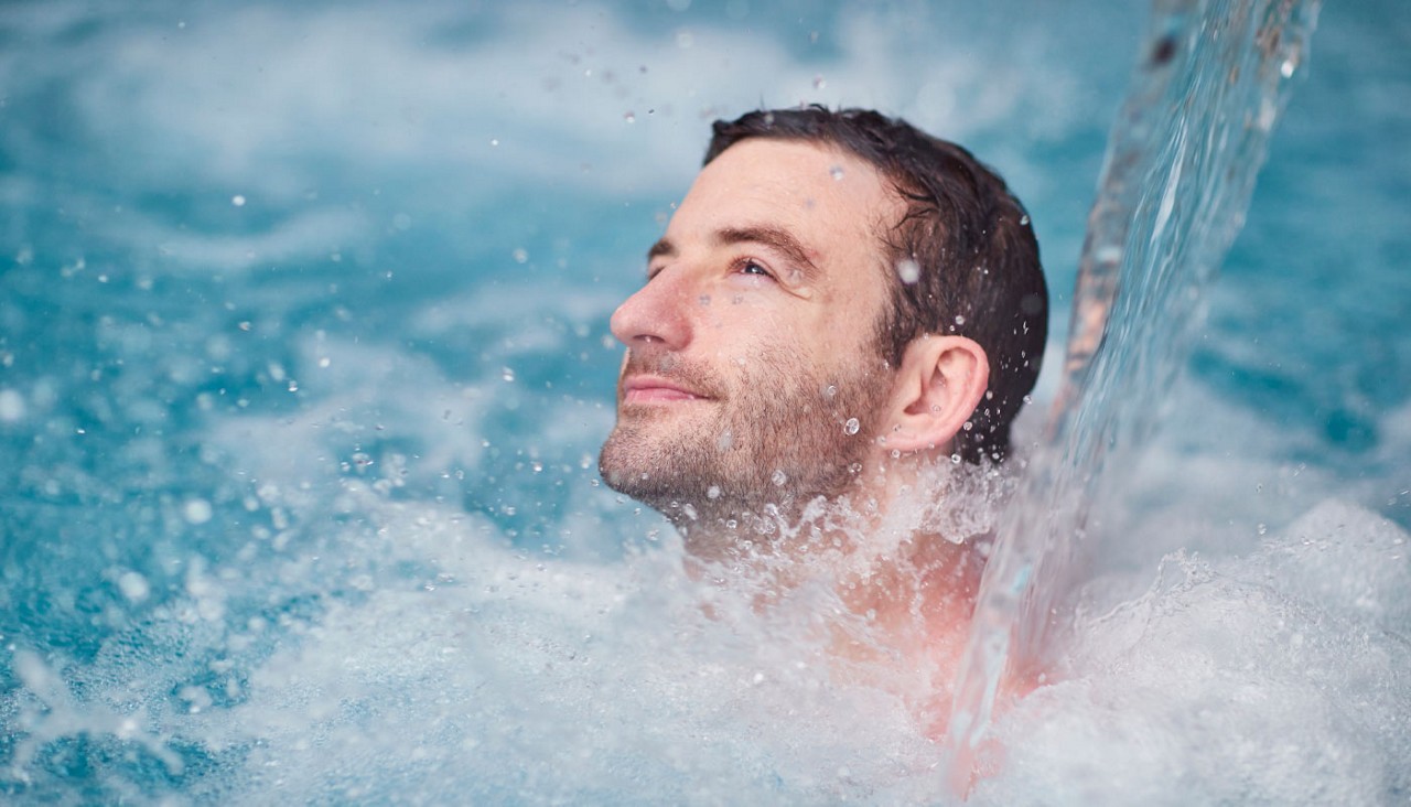 Man soaking in an Outdoor Pool underneath a flowing water fountain.